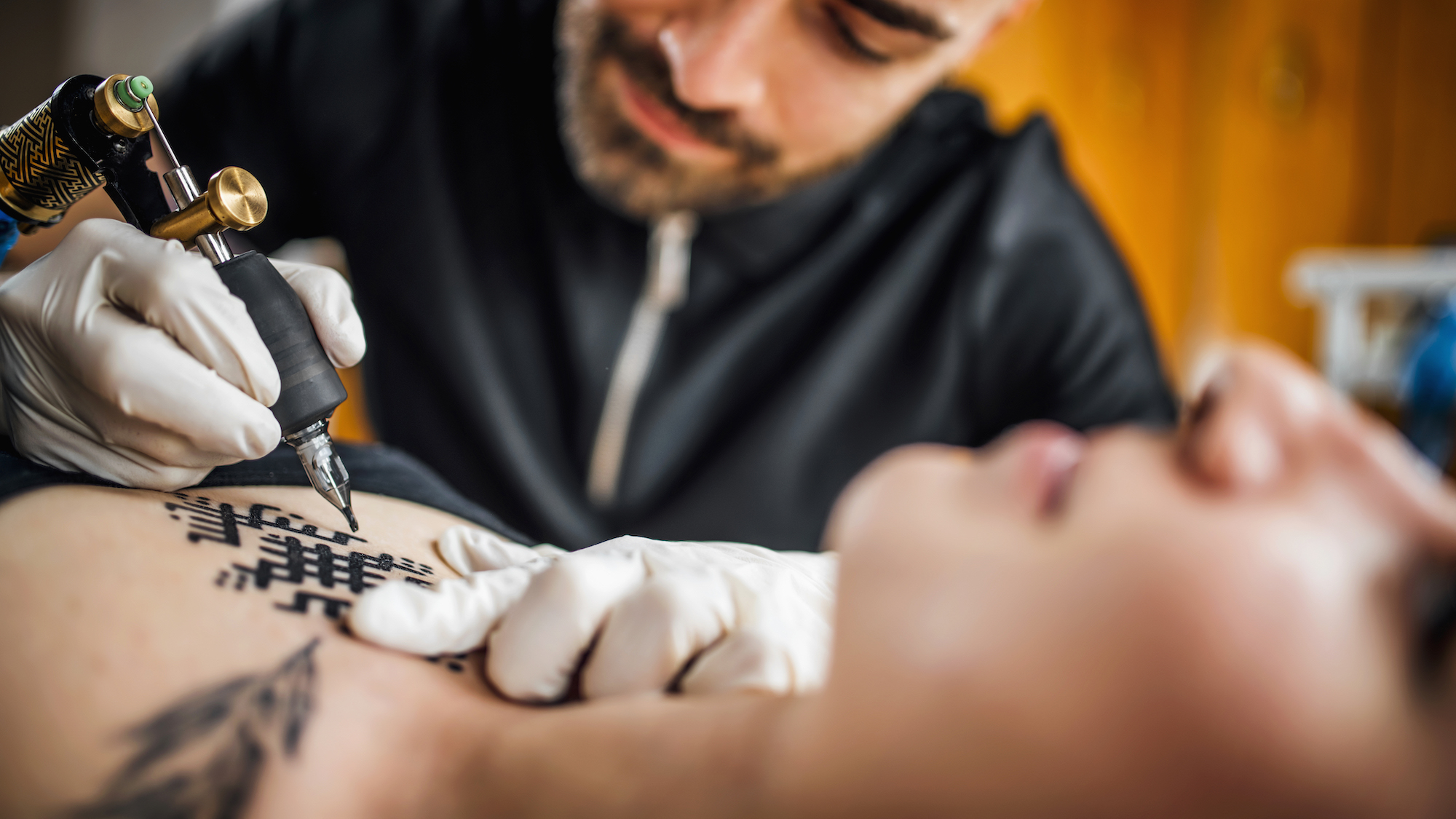 Male tattoo artist tattooing young woman in tattoo studio