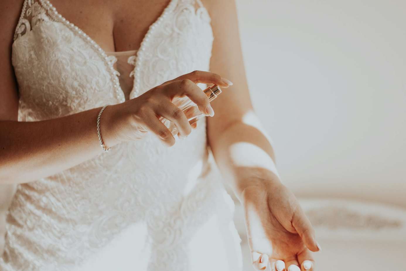 unrecognizable woman in white lacy dress spraying perfume on wrist