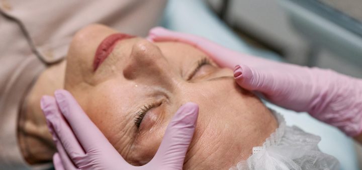 a person wearing a latex gloves touching the face of an elderly woman with her eye closed