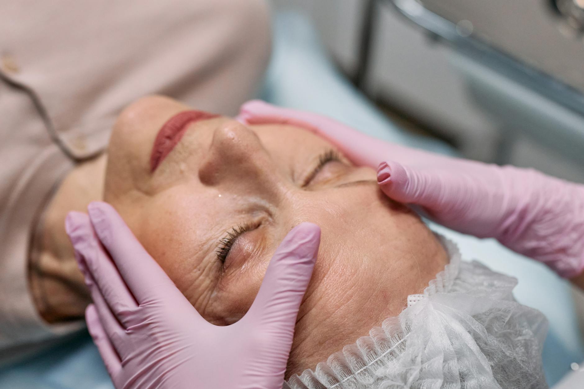 a person wearing a latex gloves touching the face of an elderly woman with her eye closed