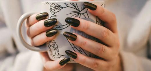 woman with black manicure holding white and grey floral ceramic cup