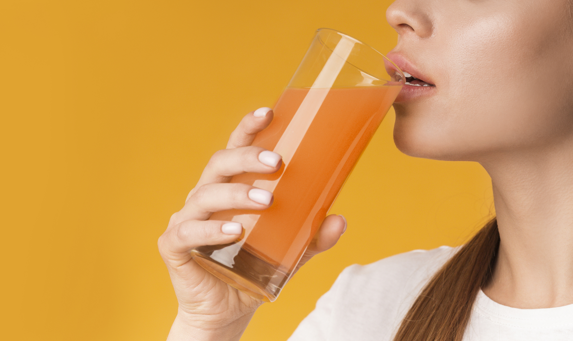 Unrecognizable woman drinking orange or carrot fresh vitamin juice, having fruit mix cocktail, standing on yellow background, cropped image, panorama