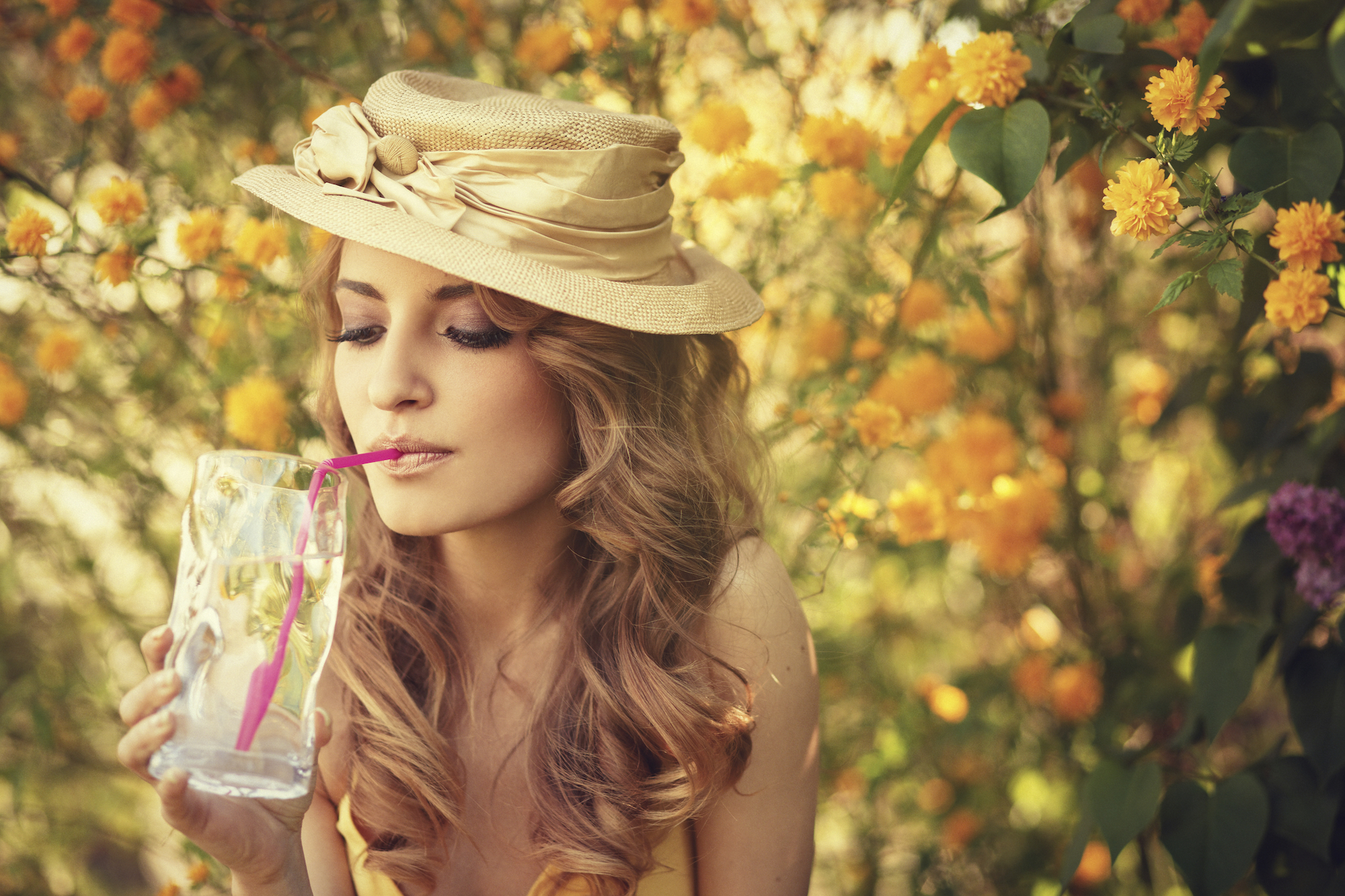 Girl with a hat drinking a glass of water with a straw