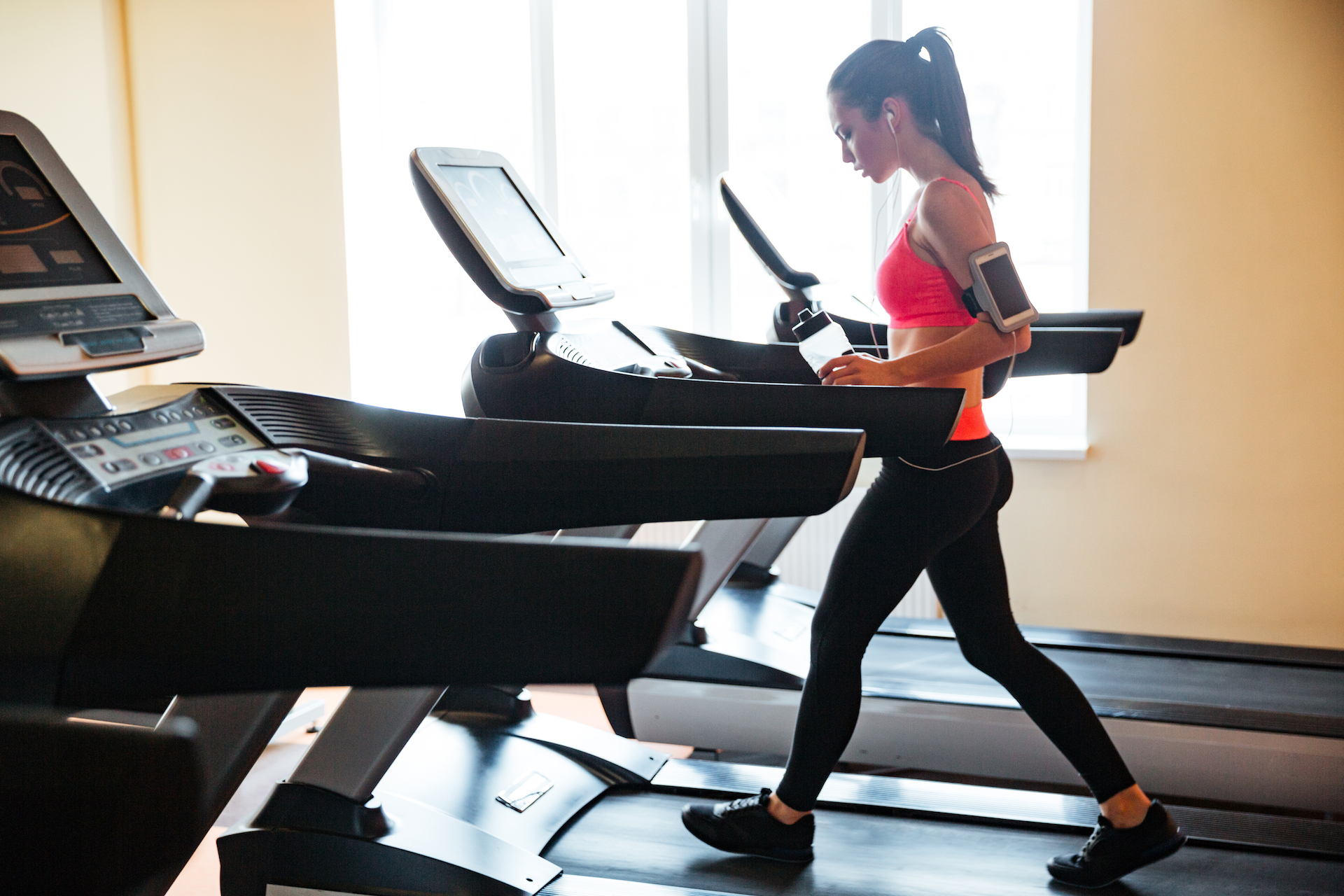 Sportswoman with earphones and blank screen smartphone using treadmill
