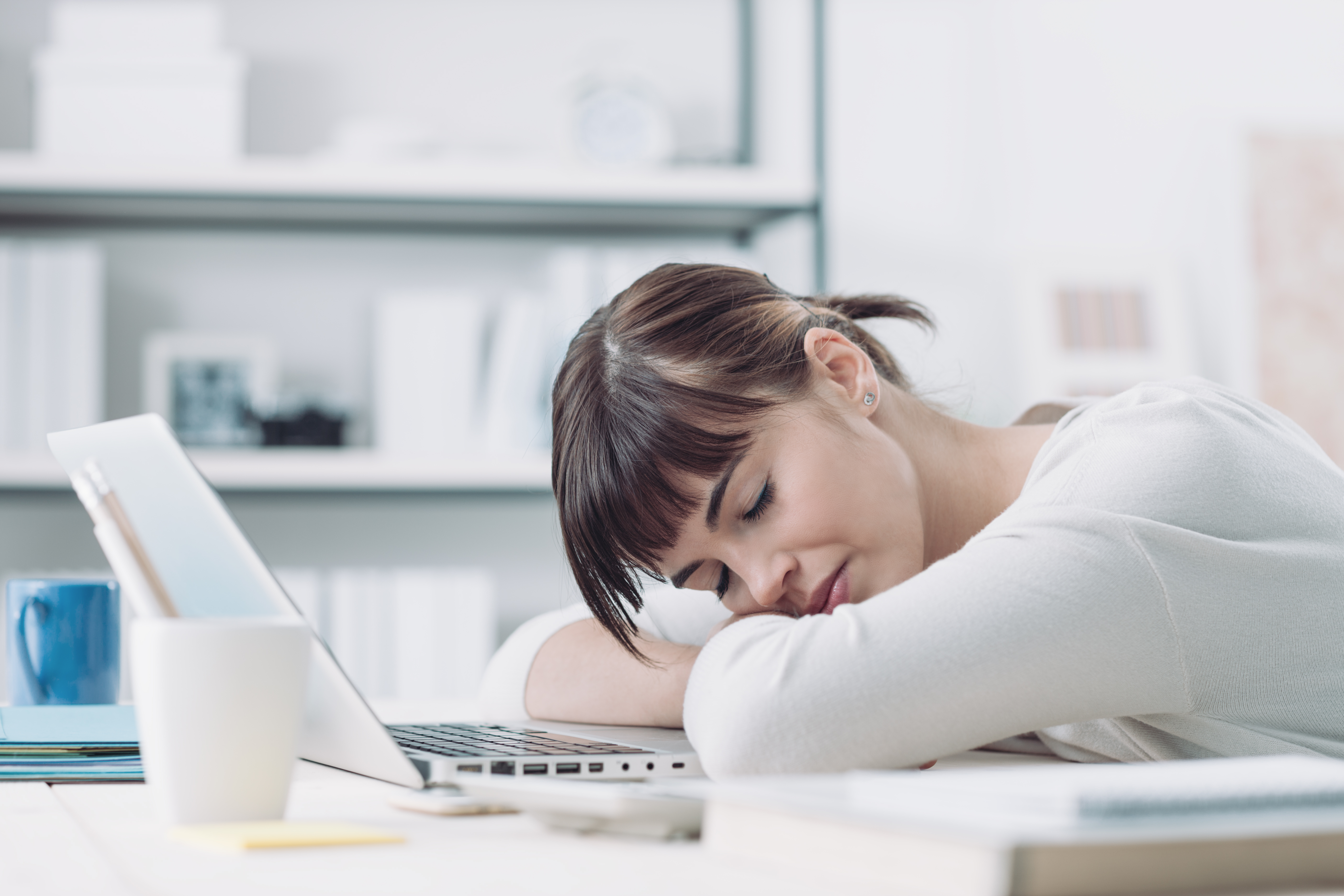 Young tired woman at office desk sleeping with eyes closed, sleep deprivation and stressful life concept