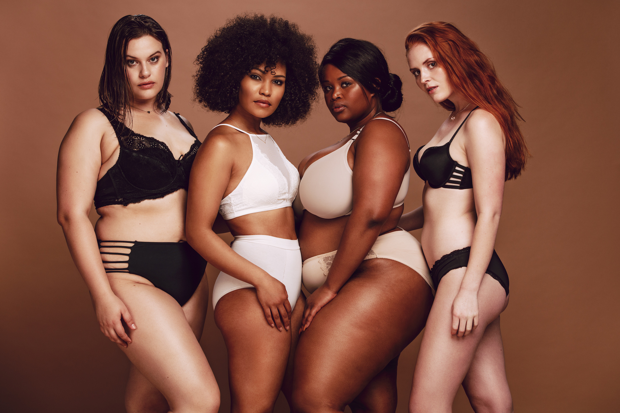 Group of different size women in lingerie looking at camera. Multi-ethnic women in different under garments posing together in studio.