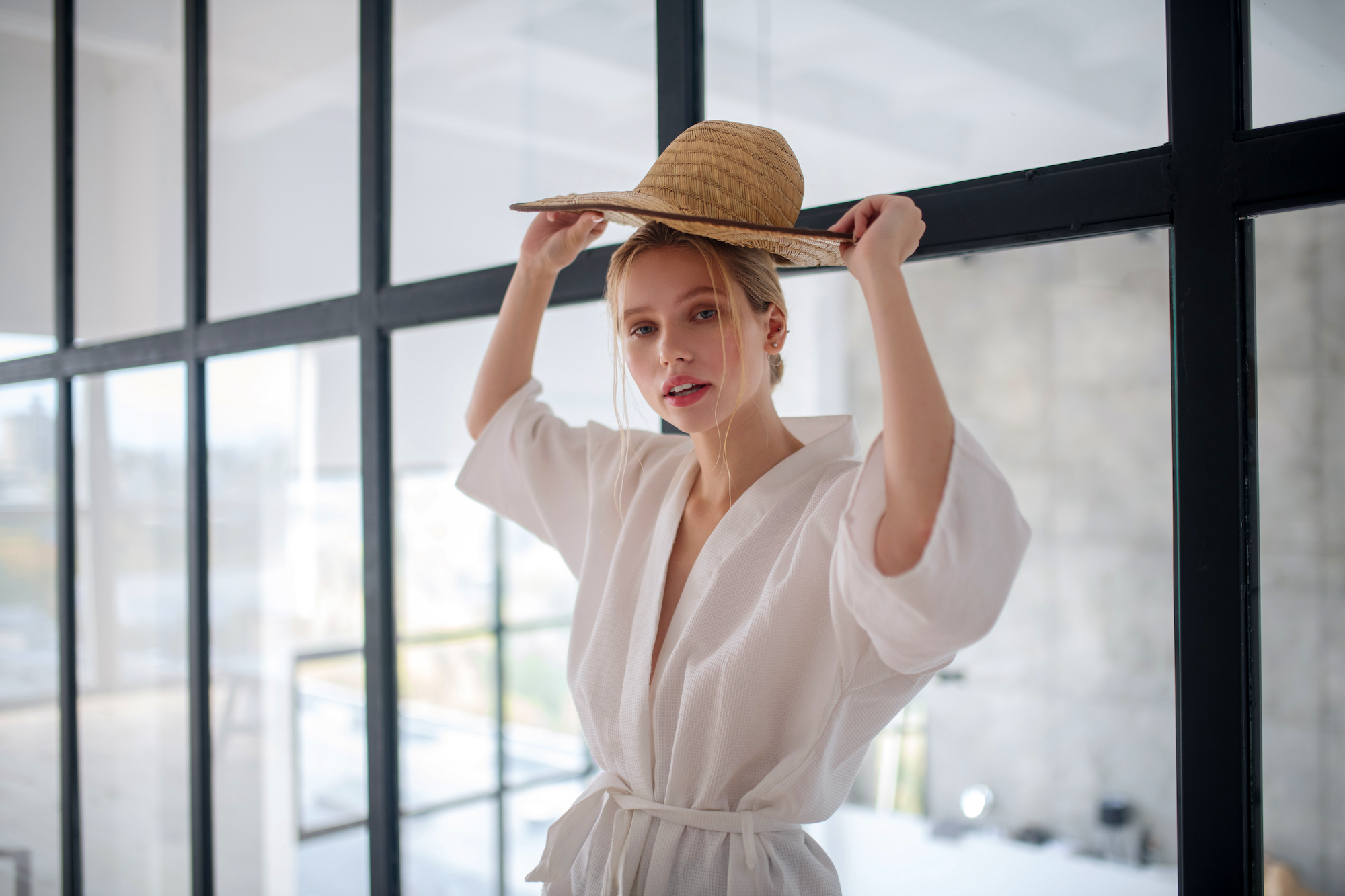 Choosing straw hat. Blonde-haired young woman holding straw hat while choosing straw hat