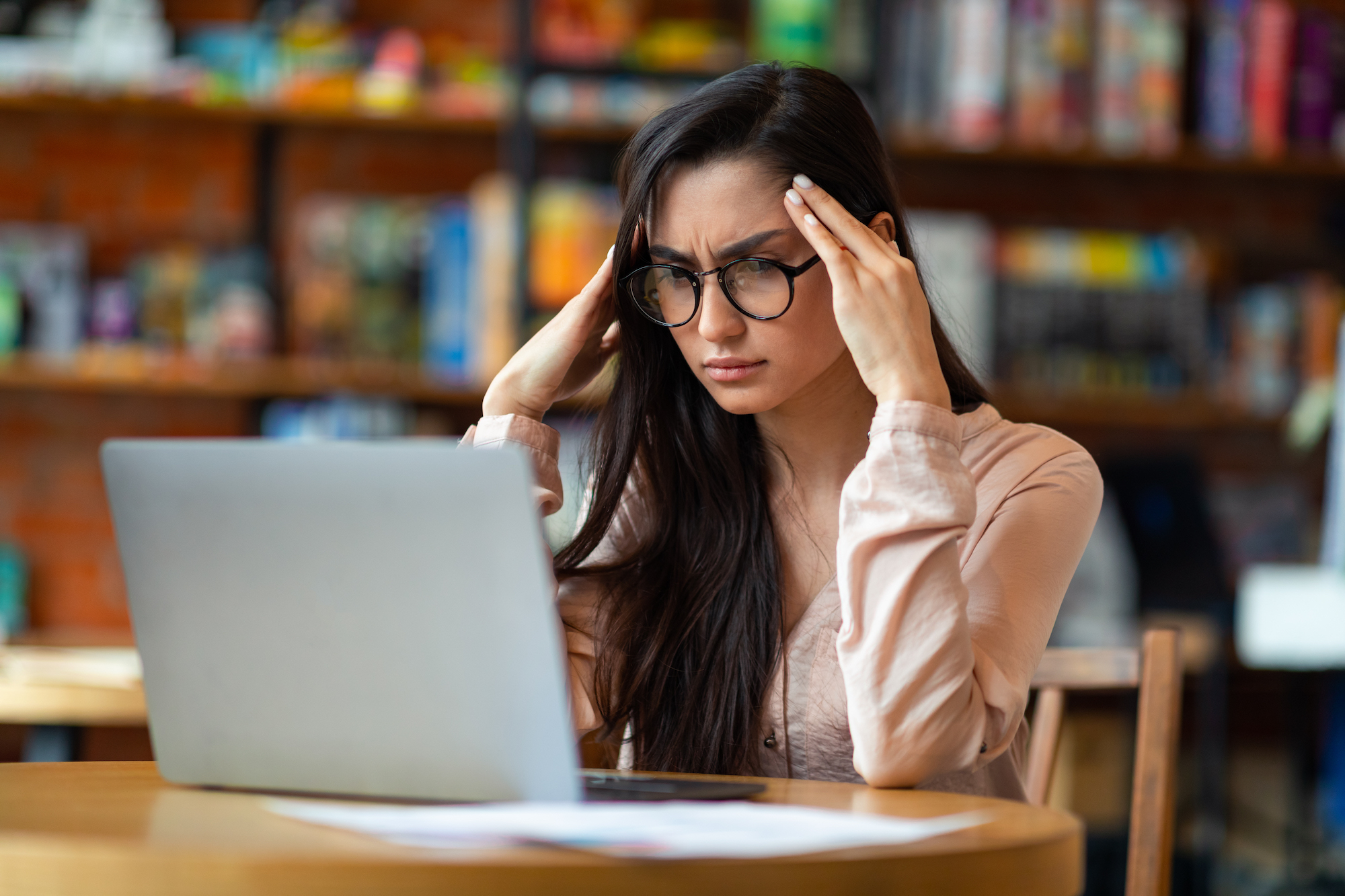 Problems at work. Exhausted latin woman freelancer tired after work on laptop, having headache, sitting at table in cafe, looking at computer screen and touching head, free space