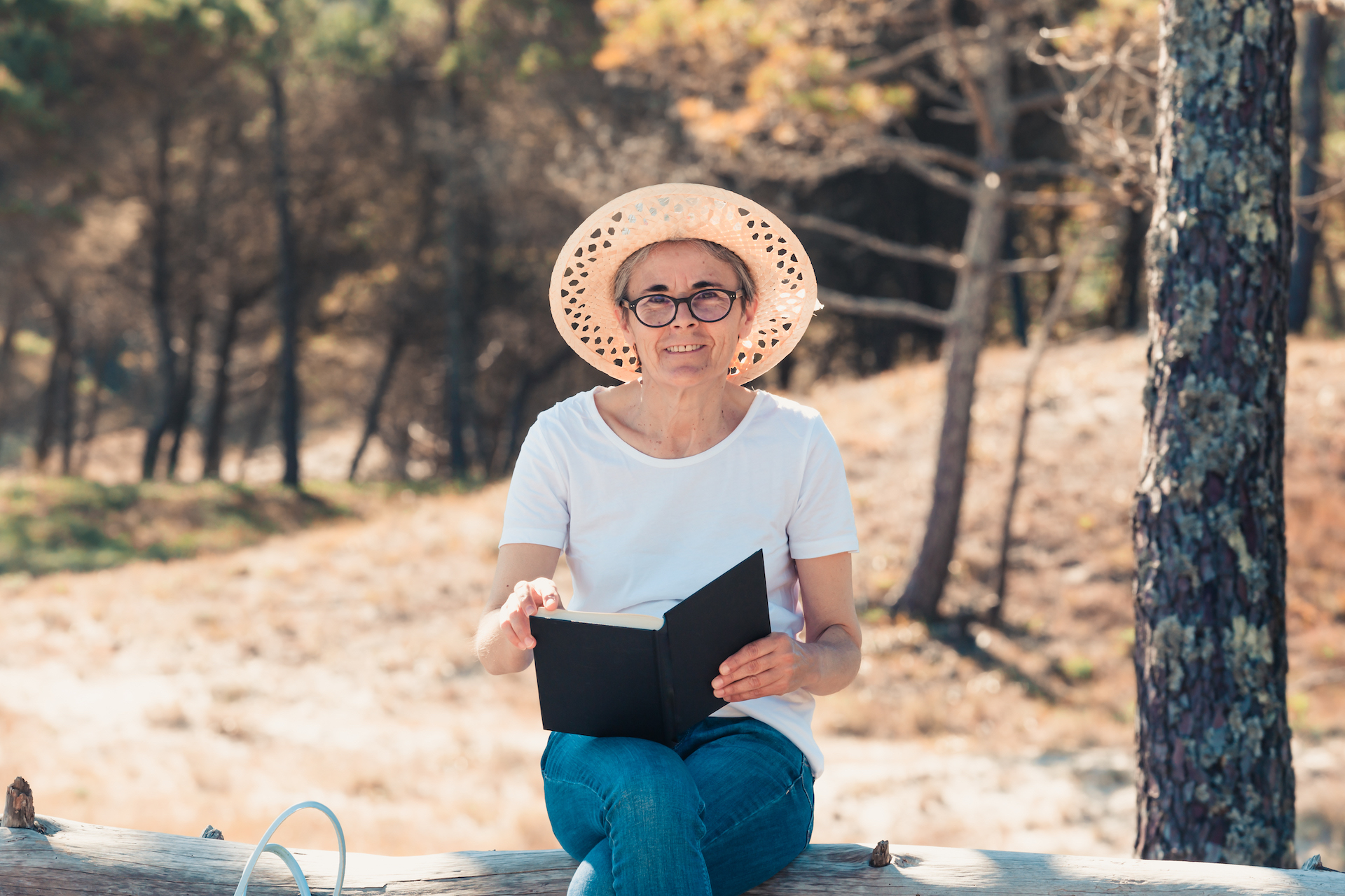 Old woman reading a book at the beach during a super sunny day. Freedom concept with copy space, relaxation and senior retirement happiness, Smiling to camera