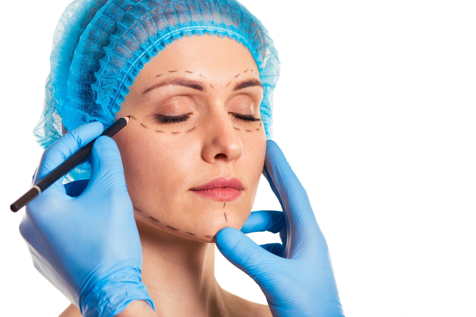 Beautiful woman in medical headwear, surgeon in medical gloves is making sketches on face, isolated on white background