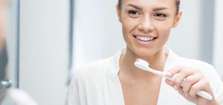 portrait of happy woman looking in mirror while brushing teeth in morning