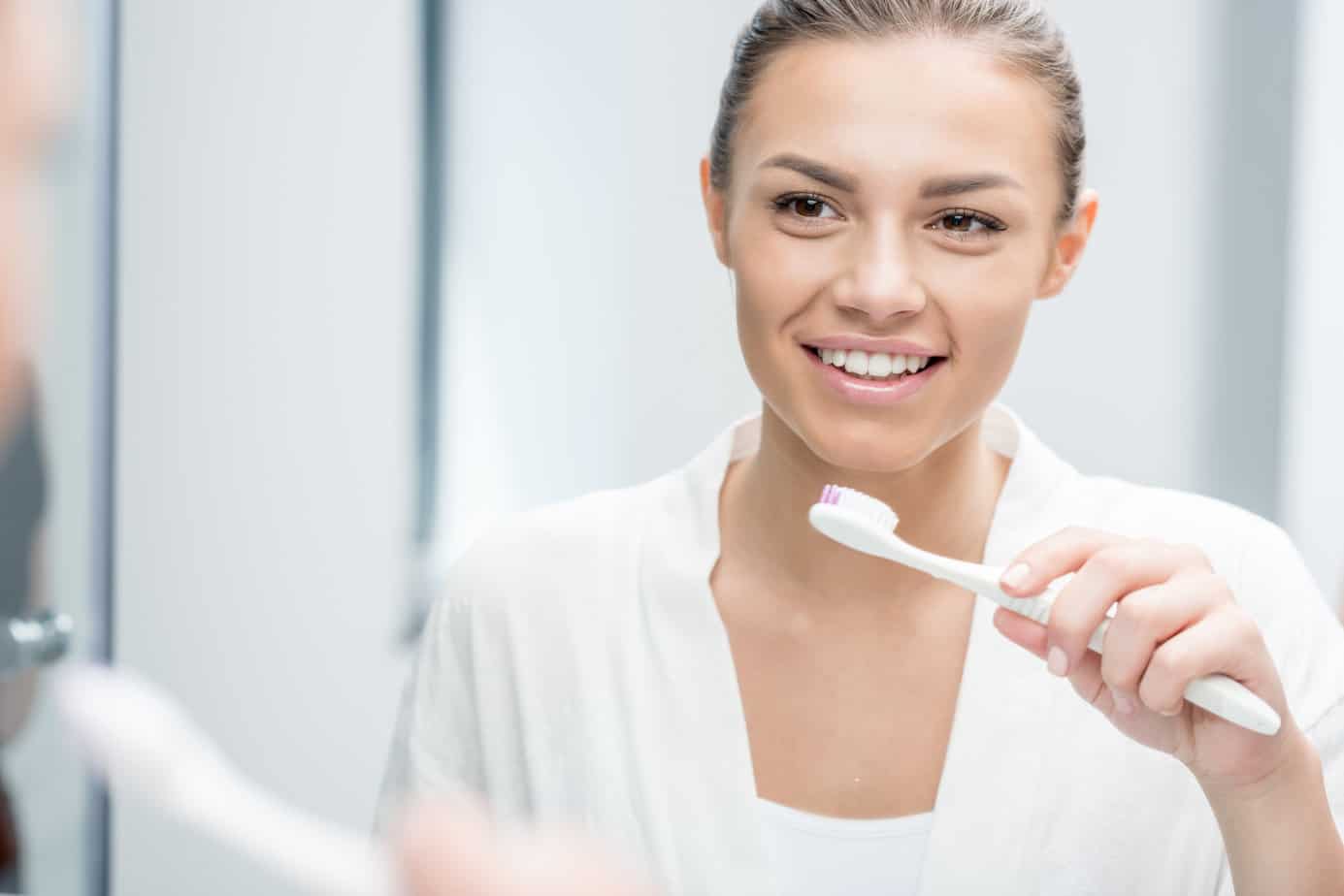 portrait of happy woman looking in mirror while brushing teeth in morning