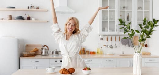 Wonderful morning, woman enjoy freshness and energy, healthy breakfast. Happy excited beautiful young european female in bathrobe raised her hands up in kitchen interior with food and tasty coffee