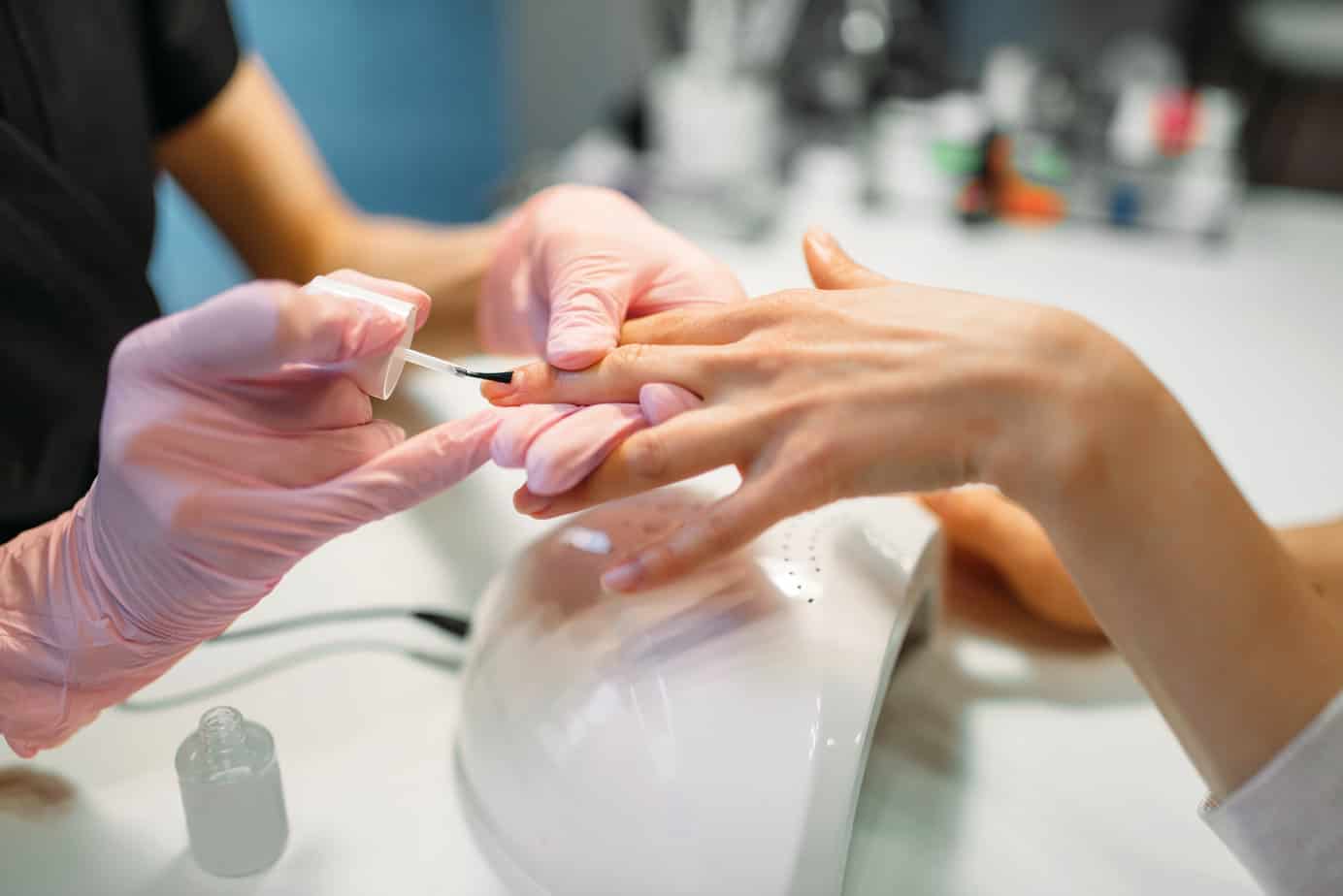 Manicure master in pink gloves applying nail varnish to female client, beauty salon. Manicurist doing fingernail care cosmetic procedure